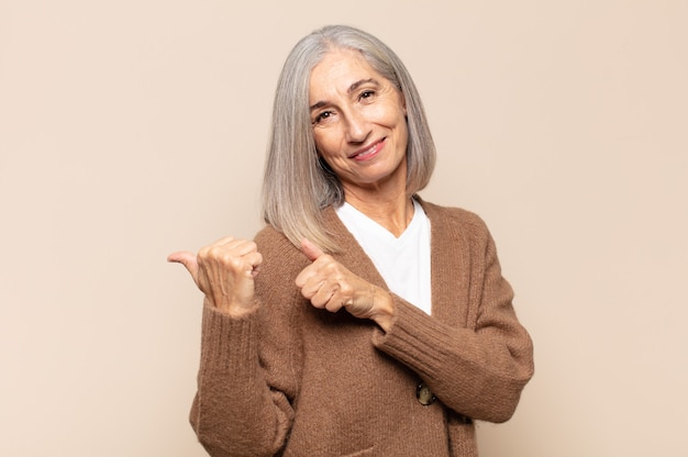 Middle age woman smiling cheerfully and casually pointing to copy space on the side, feeling happy and satisfied
