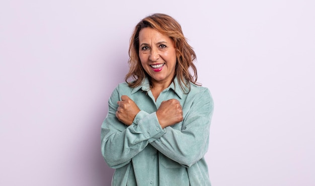 Middle age woman smiling cheerfully and celebrating, with fists clenched and arms crossed, feeling happy and positive