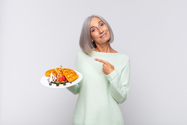 Middle age woman smiling cheerfully, feeling happy and pointing to the side and upwards, showing object in copy space. breakfast concept
