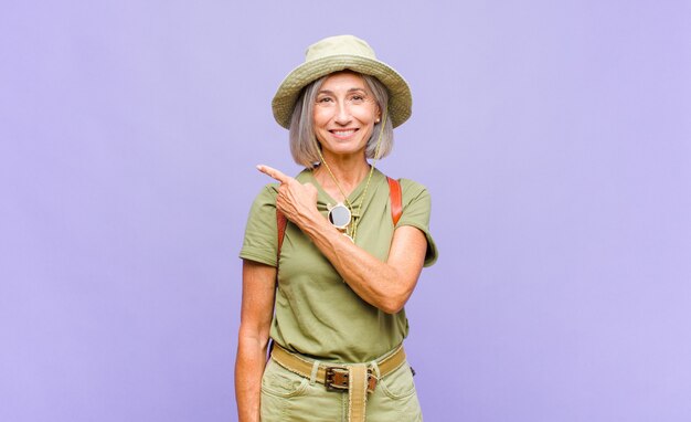 Middle age woman smiling cheerfully, feeling happy and pointing to the side and upwards, showing object in copy space