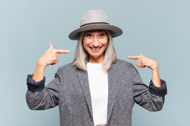 Middle age woman smiling confidently pointing to own broad smile, positive, relaxed, satisfied attitude