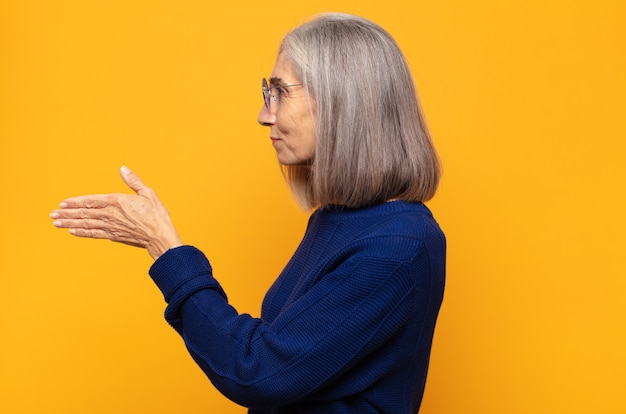 Middle age woman smiling, greeting you and offering a hand shake to close a successful deal, cooperation concept