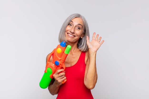 Middle age woman smiling happily and cheerfully, waving hand