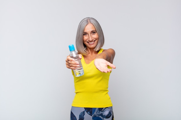 Middle age woman smiling happily with friendly, confident, positive look, offering and showing an object or concept. fitness concept