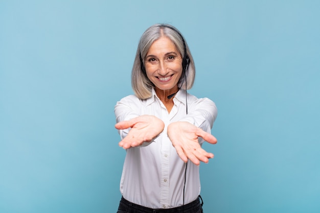 Middle age woman smiling happily with friendly, confident, positive look, offering and showing an object or concept. telemarketer concept