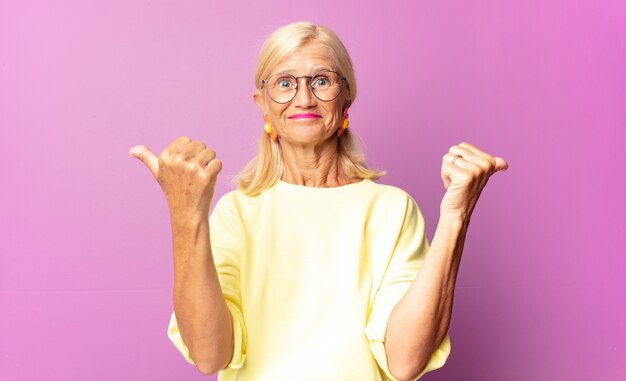 Middle age woman smiling joyfully and looking happy, feeling carefree and positive with both thumbs up