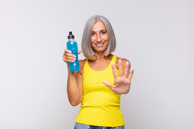 Middle age woman smiling and looking friendly, showing number five or fifth with hand