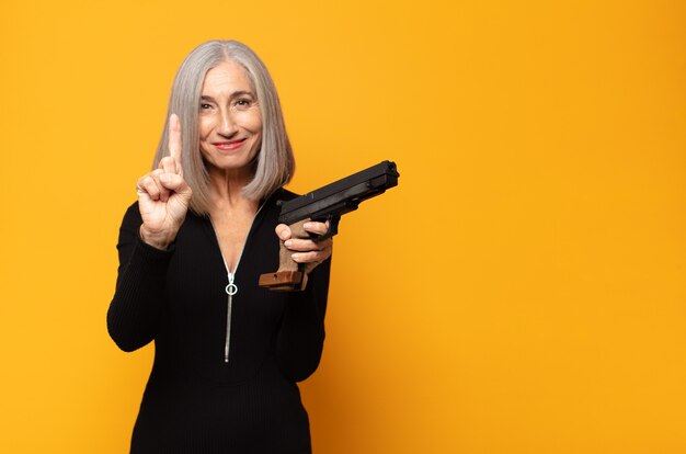 middle age woman smiling and looking friendly, showing number one or first with hand forward, counting down