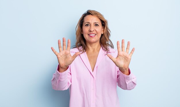 Middle age woman smiling and looking friendly, showing number ten or tenth with hand forward, counting down