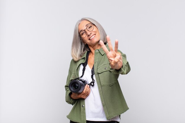 Donna di mezza età sorridente e dall'aspetto amichevole, mostrando il numero tre o terzo con la mano in avanti, il conto alla rovescia. concetto di fotografo