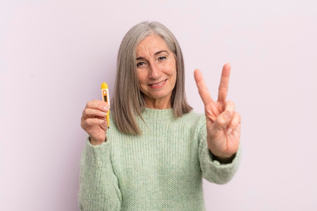 Middle age woman smiling and looking friendly showing number two medicine thermometer concept