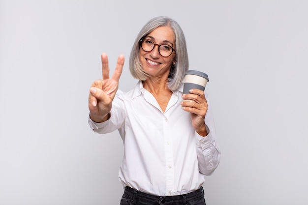 Donna di mezza età che sorride e che sembra amichevole, mostrando il numero due o il secondo con la mano in avanti, contando il concetto di caffè