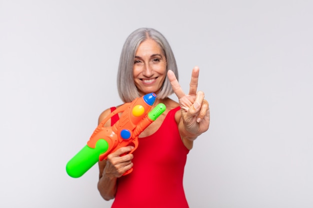 Middle age woman smiling and looking friendly, showing number two or second with hand forward, counting down with a water gun