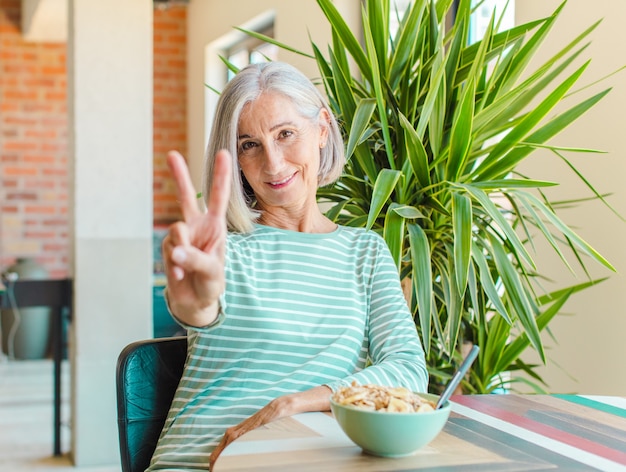 Middle age woman smiling and looking happy, carefree and positive, gesturing victory or peace with one hand