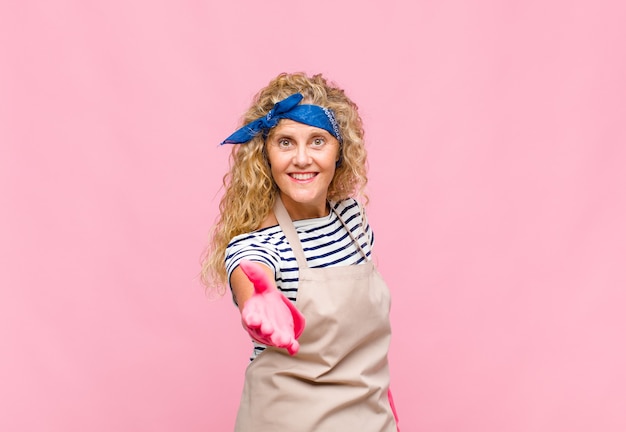 Middle age woman smiling, looking happy, confident and friendly, offering a handshake to close a deal, cooperating housekeeper concept