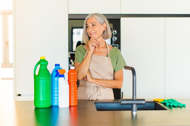 Middle age woman smiling with a happy, confident expression with hand on chin, wondering and looking to the side