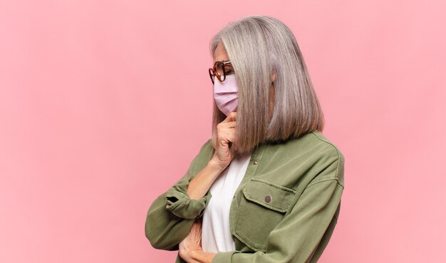 Middle age woman smiling with a happy, confident expression with hand on chin, wondering and looking to the side