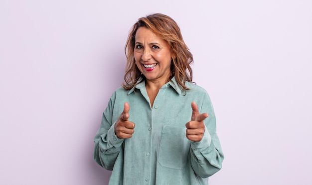 Middle age woman smiling with a positive, successful, happy attitude pointing to the camera, making gun sign with hands