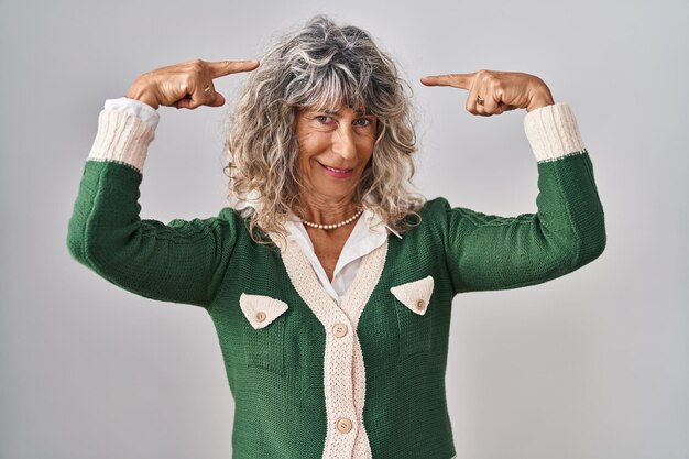 Middle age woman standing over white background smiling pointing to head with both hands finger great idea or thought good memory