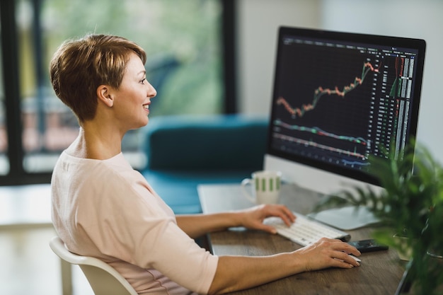 Middle age woman trading with cryptocurrency while working on computer at home office.She is monitors her investments in the stock markets.