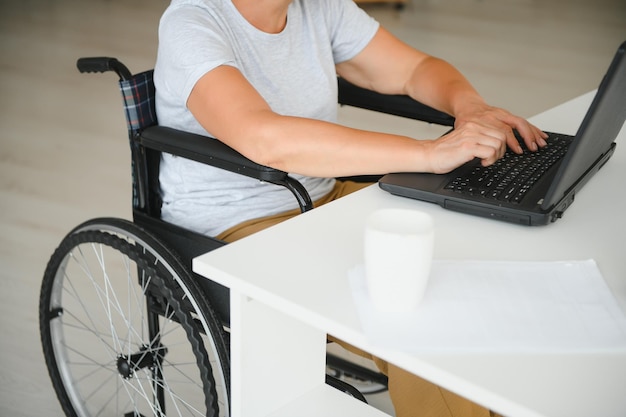 Middle age woman using laptop sitting on wheelchair at home