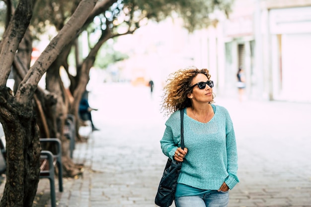 도시 야외 공원을 걷는 중년 여성은 쇼핑을 위해 여가 활동을 하는 행복한 캐주얼 옷 파란색 스웨터 여성 사람들을 웃고 있습니다.