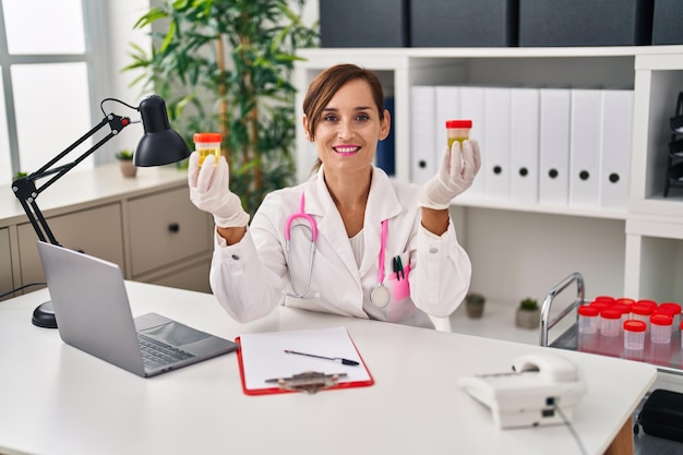 Middle age woman wearing doctor uniform holding urine analysis test tubes at clinic