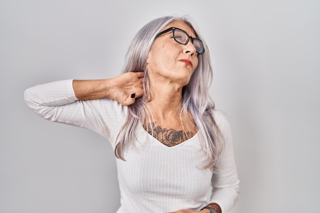 흰색 배경 위에 서 있는 회색 머리를 가진 중년 여성은 손 근육통으로 목을 만지는 목 통증 부상의 고통