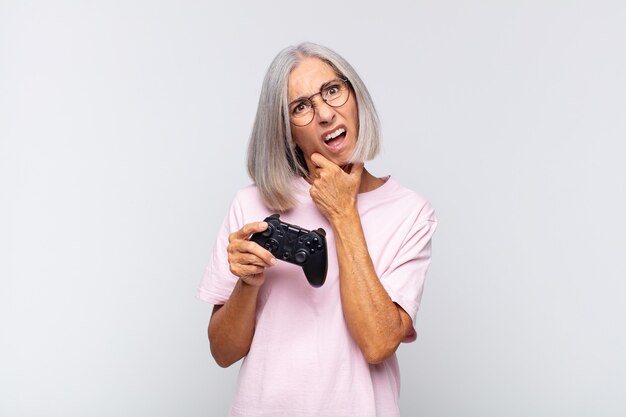 Middle age woman with mouth and eyes wide open and hand on chin, feeling unpleasantly shocked, saying what or wow. playing console concept