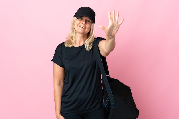 Middle age woman with sport bag isolated on pink wall counting five with fingers