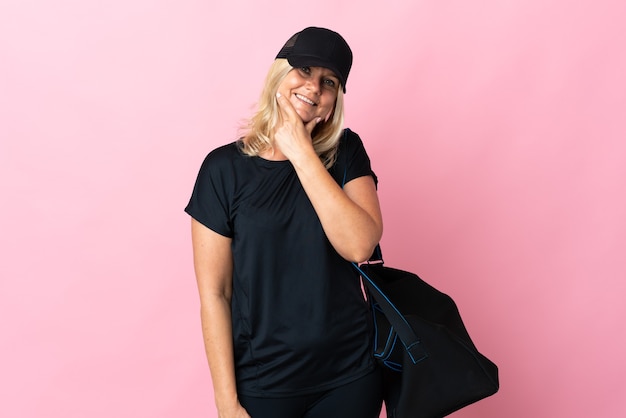 Женщина среднего возраста со спортивной сумкой, изолированной на розовой стене, счастливая и улыбающаяся