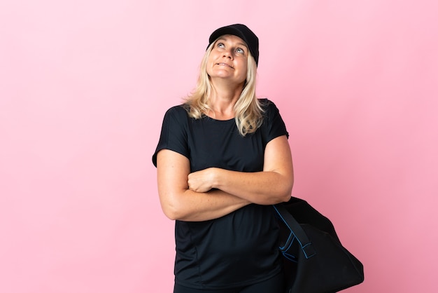 Женщина среднего возраста со спортивной сумкой изолирована на розовой стене и смотрит вверх