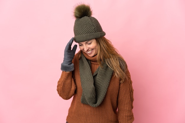 Middle age woman with winter hat isolated on pink laughing