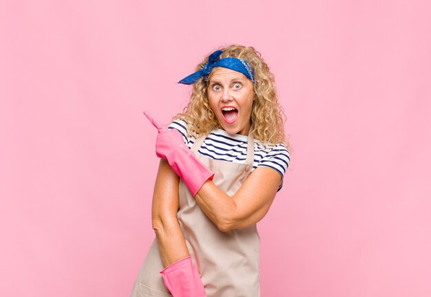 Middle age womanlooking excited and surprised pointing to the side and upwards to copy space housekeeper concept