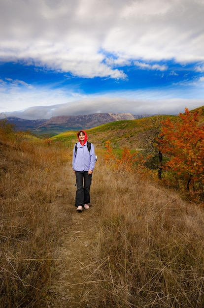 Middle aged active caucasian female model with backpack walk in mountains autumn time