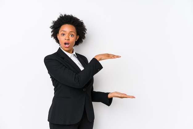 Middle aged african american business  woman against a white background isolated shocked and amazed holding a copy space between hands.