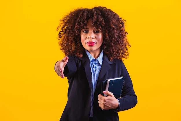 Middle aged african american business woman against a yellow background isolated stretching hand at camera in greeting gesture.