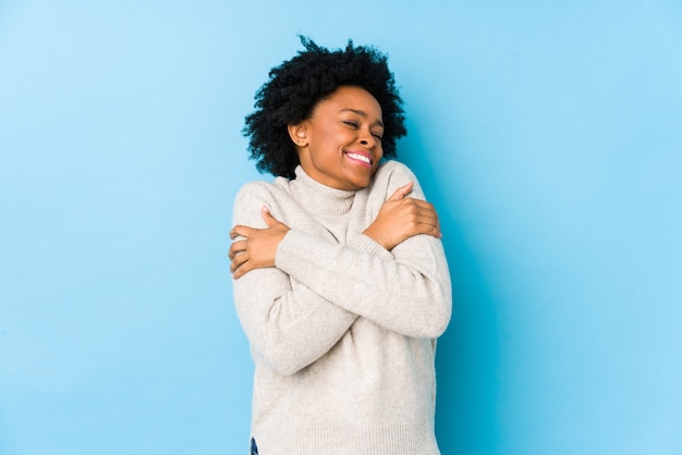 Middle aged african american woman against a blue isolated hugs, smiling carefree and happy.