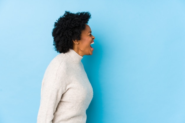 Middle aged african american woman against a blue space isolated shouting towards a copy space