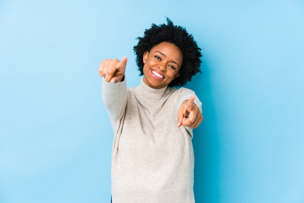 La donna afroamericana di mezza età contro una parete blu ha isolato i sorrisi allegri che indicano la parte anteriore.