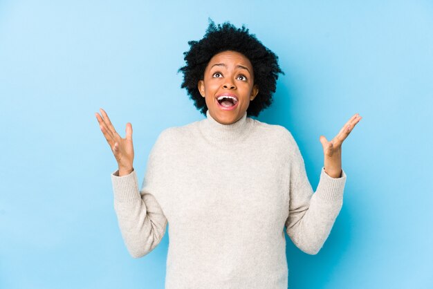 Middle aged african american woman against a blue wall isolated screaming to the sky, looking up, frustrated.