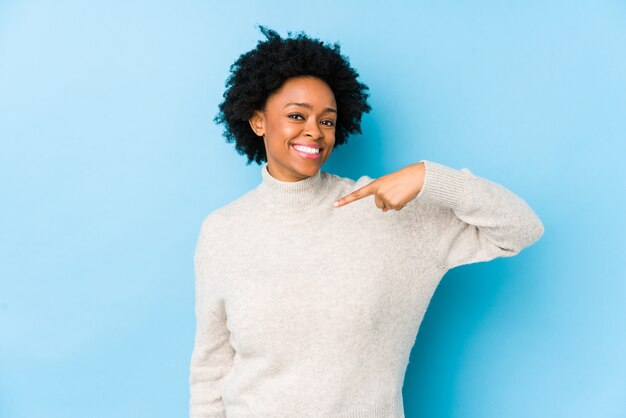 Middle aged african american woman against a blue wall person pointing by hand to a shirt blank space, proud and confident