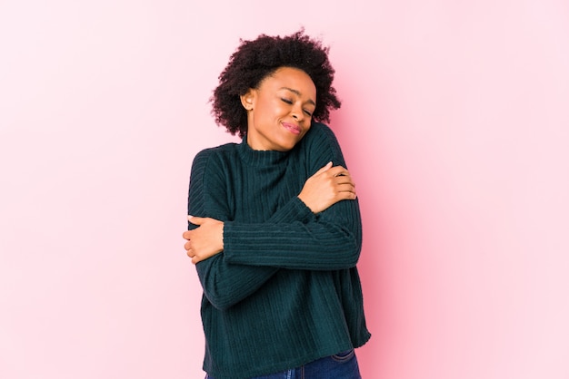 Photo middle aged african american woman against a pink wall isolated hugs, smiling carefree and happy.