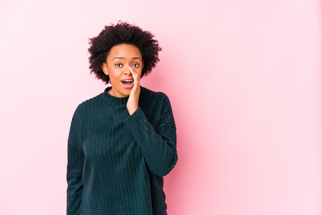 Middle aged african american woman against a pink wall isolated is saying a secret hot braking news and looking aside