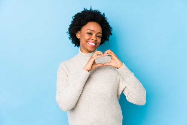 Middle aged african american woman smiling and showing a heart shape with hands.