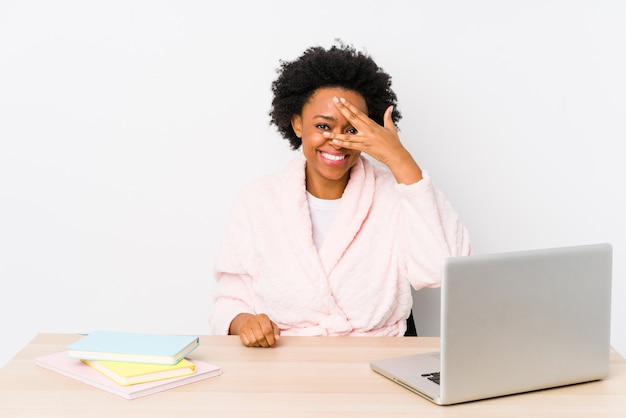 Middle aged african american woman working at home isolated blink at through fingers, embarrassed covering face.