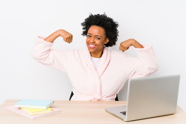 Middle aged african american woman working at home showing strength gesture with arms