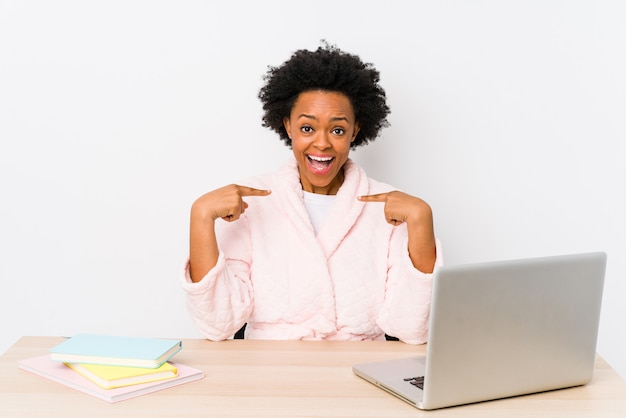 Middle aged african american woman working at home surprised pointing with finger, smiling broadly.