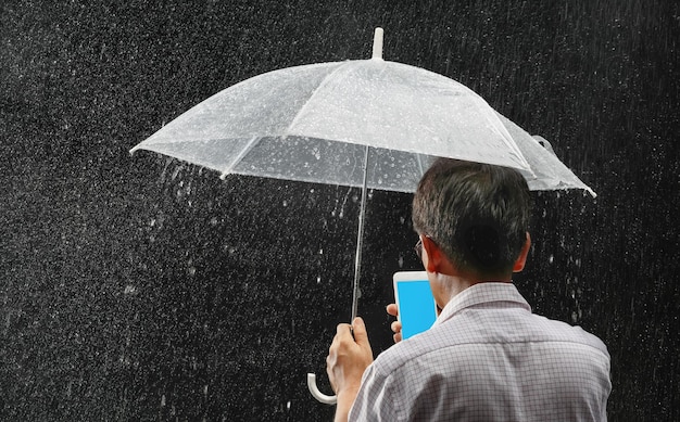 夜の雨の下で彼の傘と電話を保持している中年のアジア人男性