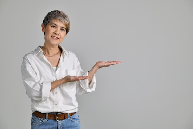 Middle aged Asian woman showing empty copy space on the open hands palm for text or product isolated on white background. looking at the camera